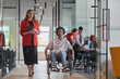 © .shock - A group of young business people in a modern glass-walled office captures the essence of diversity and collaboration, while two colleagues, including an African American businessman in a wheelchair