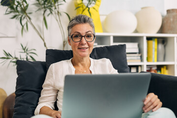 Senior woman with glasses is using a laptop at home.