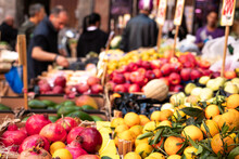 Fruit And Vegetable Stall In A Street Market In Naples In Italy. Signs With Prices In The Background, Oranges, Bananas, Pomegranates.