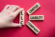 © Natallia - LLC - Limited liability company. Wooden cubes with word LLC. Businessman hand. Beautiful red background. Business and LLC concept. Copy space.