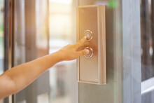 Close-up Of Child's Finger Presses Chrome Button To Call Elevator In Modern Residential Building. Human Hand Reaches For Buttons Of Lift Call, Sunshine Backdrop. Up To High Floor. Copy Ad Text Space