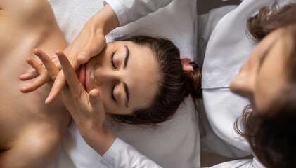 Wall Mural - Top view of a qualified massotherapist woman's hands massaging female client facial skin. Beauty treatment concept.