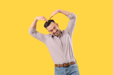 Wall Mural - Handsome man making heart with his hands on yellow background