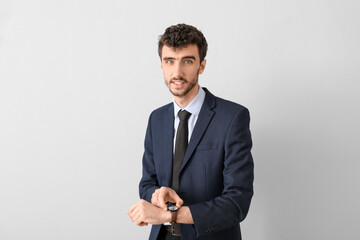 Wall Mural - Young businessman in suit with wristwatch on light background