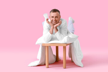 Wall Mural - Mature man with soft pillow and blanket lying on pink background