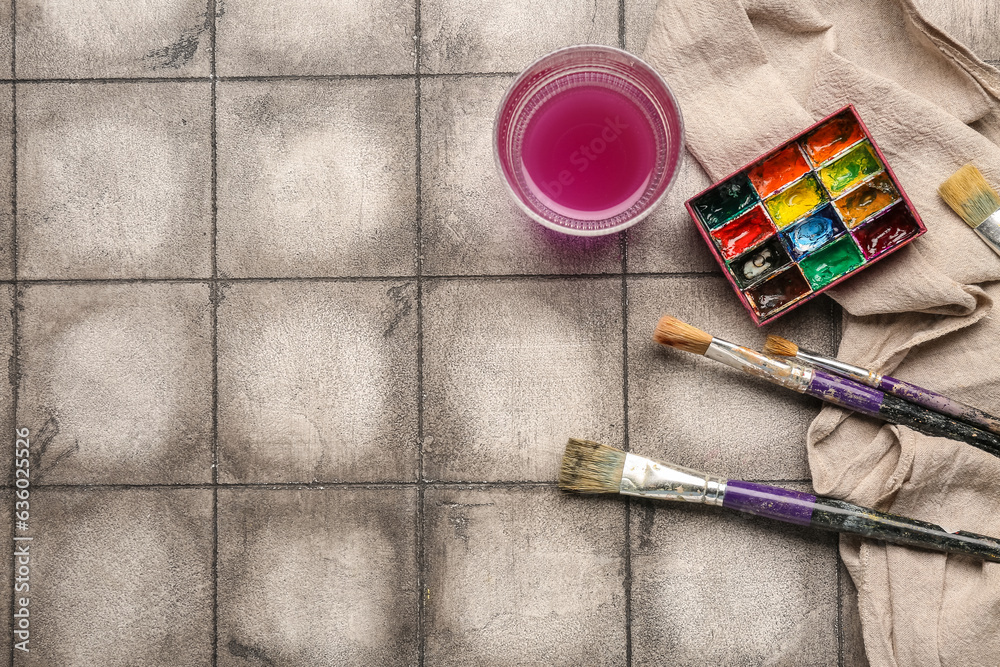 Artist's paints with brushes, cloth and glass on grey tile background