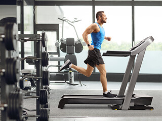 Poster - Muscular man running on a treadmill at the gym