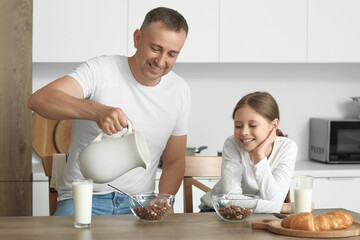 Canvas Print - Little girl with her father eating corn balls and drinking milk at table in kitchen