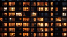 Lit Windows Of Tall Apartment Building At Night Urban Backdrop. Silhouette Concept