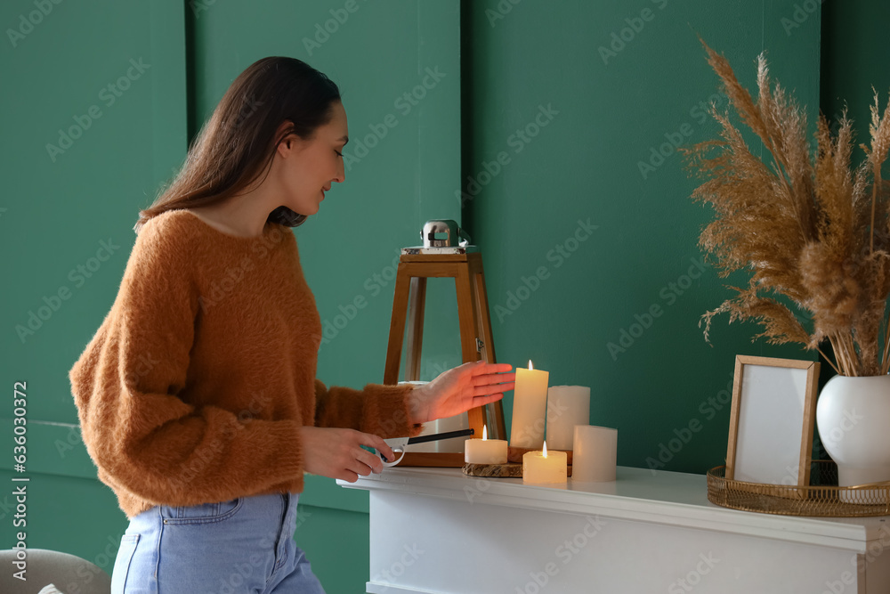 Young woman lighting candle on mantelpiece at home