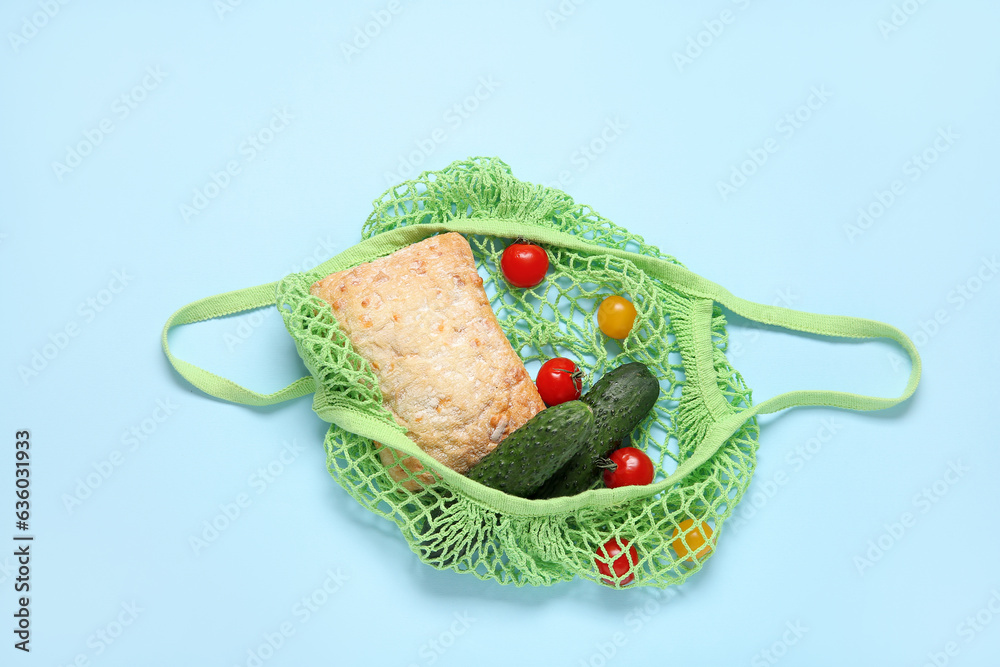 Mesh bag with fresh vegetables and bread on blue background