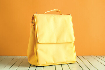 Yellow lunch box bag on green wooden table near orange wall