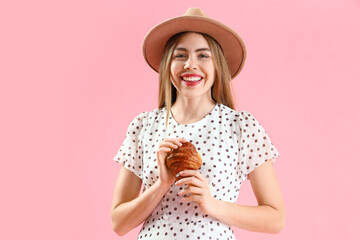 Sticker - Beautiful young woman in wicker hat with tasty croissant on pink background