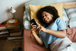 © BONNINSTUDIO/Stocksy - Teen girl using phone in bed