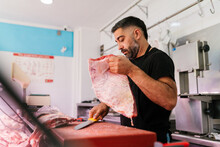 Focused Man Cutting Piece Of Meat In Shop