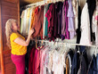 © Shava Cueva/Stocksy - Woman in yellow shirt select clothes from a closet
