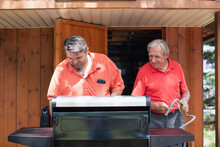Father And Son Helping Each Other Fire Up A Grill.