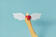 Paper Craft Hand Holding Red Heart With White Wings.
