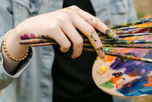 Close Up Of Hand Holding Paint Brushes With Colorful Palette 