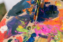 Close Up Pf Paint Brushes With Colourful  Paint Palette Behind 