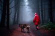 Young woman in a red raincoat walking with a wolf in dark forest