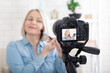 © missty - Woman doing makeup demonstrating cosmetics and shooting herself on video camera. Selective focus.