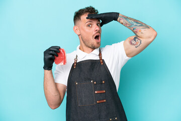 Wall Mural - Butcher caucasian man wearing an apron and serving fresh cut meat isolated on blue background doing surprise gesture while looking to the side