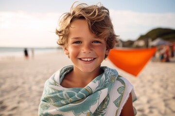 Portrait of smiling little boy with beach towel on the beach at sunset