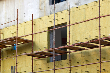 Poster - scaffolding on иuilding for thermal insulation with mineral wool. Facade wall insulation and installing new windows. Wall insulation, building construction, finishing works.