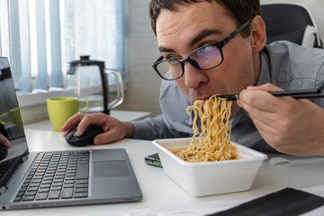 male worker busy working with laptop, use chopsticks to hastily eat instant noodles during office lu