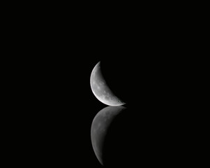 Wall Mural - waning crescent moon with warped reflection on black background 7-11-2020