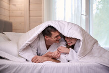 Happy couple in bathrobes with blanket covering heads on bed