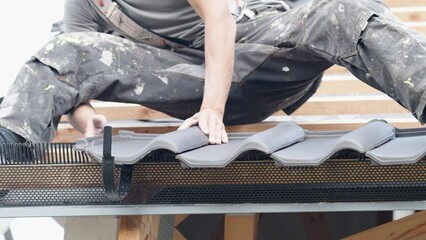 Wall Mural - the hands of a professional craftsman are laying burnt roofing tiles on the roof of a new building