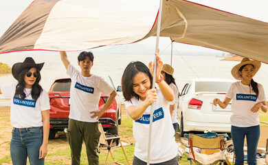 Volunteer groups of young men and women cheering,together set up tents to shade from the hot summer sun during a volunteer camp to help society collect garbage in natural water sources.