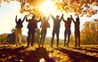 © Studio Romantic - Unity and friendship. Group of friends holding hands raise them up while standing in sunlight in autumn park. Rear view of people in casual clothes standing with backs to camera and holding hands.