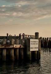 Canvas Print - Vertical shot of a weathered wooden pier jutting out into a tranquil blue body of water