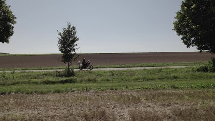 Sticker - Aerial video of a motorcyclist on the road surrounded by trees and farm fields