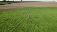 Aerial Video Of A Man Running In The Green Field With His Black Dog
