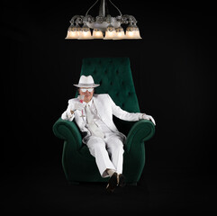 Poster - rich man in a white suit sits in a chair, black studio background