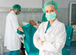 © Dorde - Portrait of female medical worker in hospital ward wearing protective mask standing with arms crossed with her team helping pregnant woman to give birth.