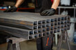 stack​ of square​ metal tubes​ profile or pipes for construction supplies and welding works with worker on background