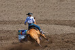 A cowgirl is riding a horse in a rodeo. She is competing in a barrel racing contest. The horse is kicking up a lot of dirt rounding the barrel. The horse is brown and the cowgirl is wearing blue.