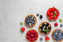 Tartlets With Different Fresh Berries On Light Grey Table, Flat Lay And Space For Text. Delicious Dessert