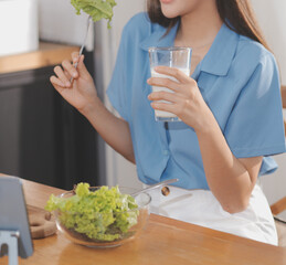 A young woman with a beautiful face in a blue shirt with long hair eating fruit sitting inside the kitchen at home with a laptop and notebook for relaxation, Concept Vacation.