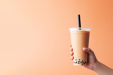 A hand holding takeaway plastic cup of delicious iced bubble milk tea and black pearls with copy space