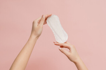 Sanitary napkin in woman's hand on pink background