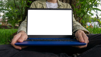 A man sits on the grass at a computer with a white screen.