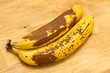 Dojrzałe banany z brązową skórką leżą na drewnianym blacie kuchennym
