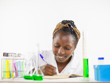 Young Female Scientist Writting Down Something On Her Notebook While Performing An Experiment In A Laboratory