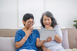 © wichayada - Two old female besties are watching a online media on a tablet while relaxing in the living room together.